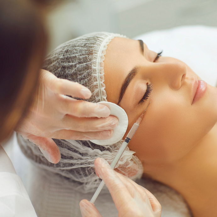 Corrección de ojeras Joven con los ojos cerrados y una malla blanca en el pelo mientras un experto le suministra un compuesto para su tratamiento de belleza